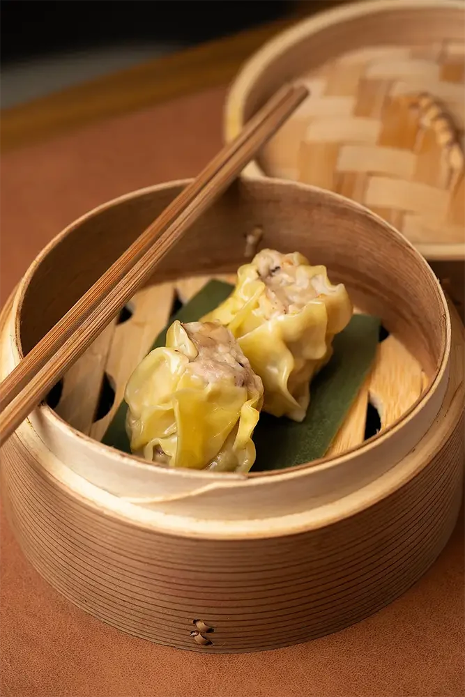 Dim sum de tamales de cerdo en caja de bambú con palillos.