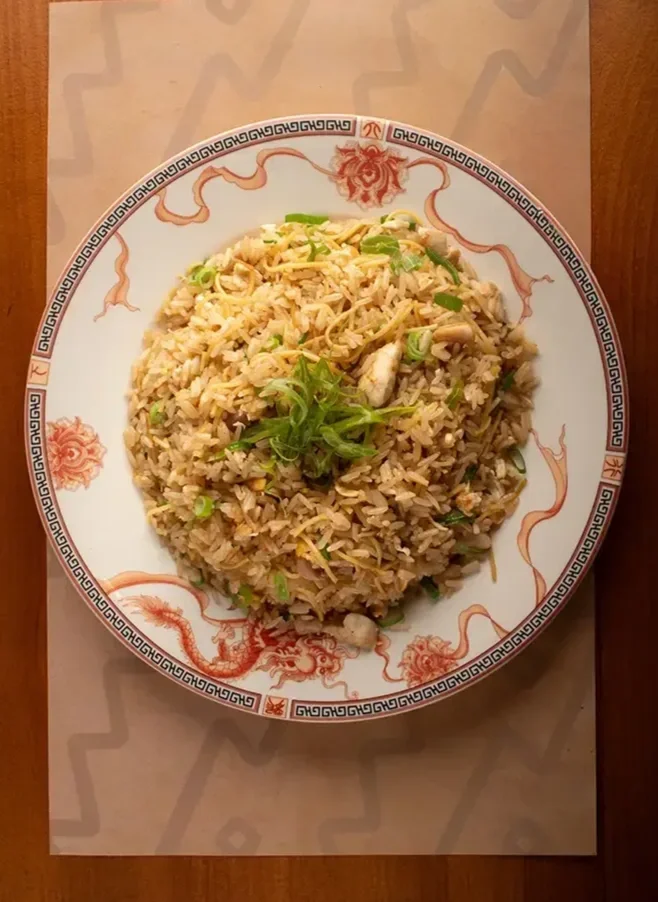 Arroz frito con cebolla, pollo y verduras en plato decorado con dragón, en mesa de madera.
