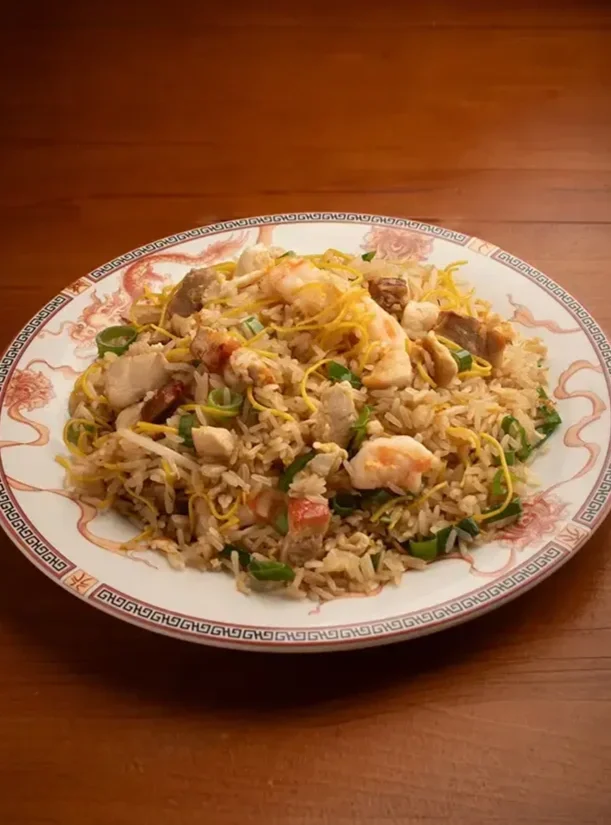Plato de arroz frito con mariscos, pollo, huevo, cebolla y cebollín en un plato decorativo chino sobre una mesa de madera.