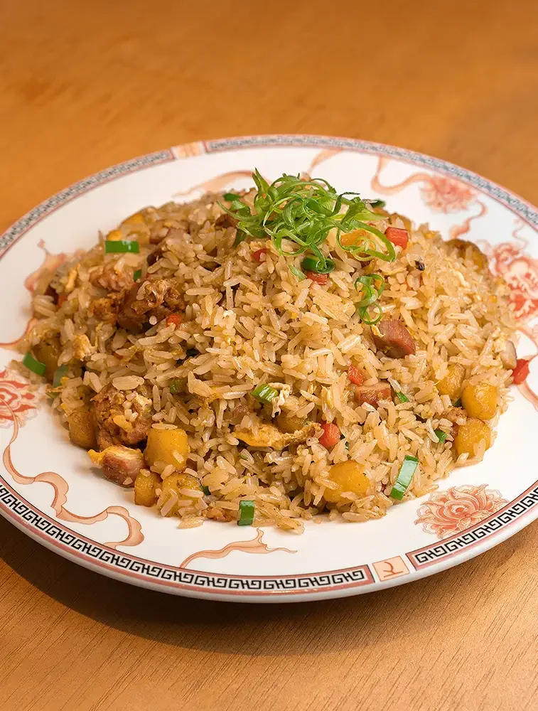 Arroz frito con verduras y carne, servido en un plato decorativo con cebollín picado en la parte superior.