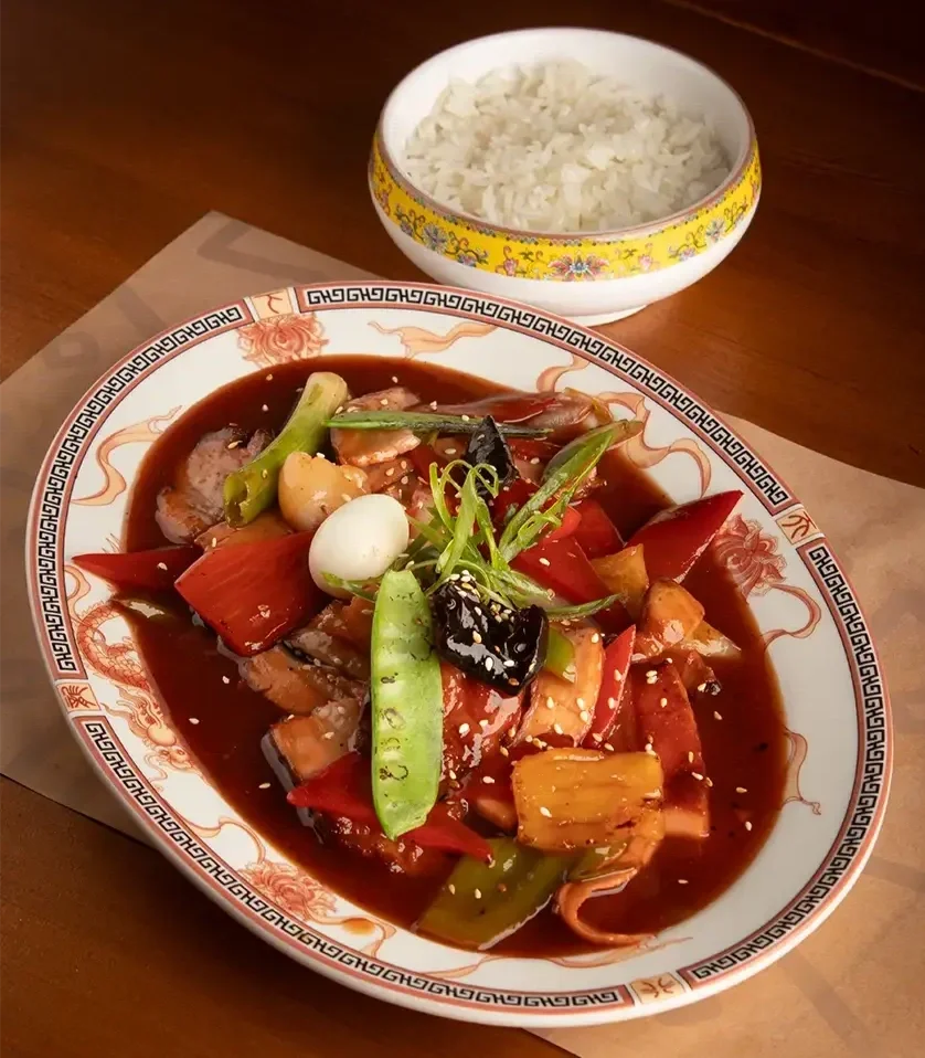 Plato de comida china con carne y verduras en salsa, acompañado de arroz en un bol