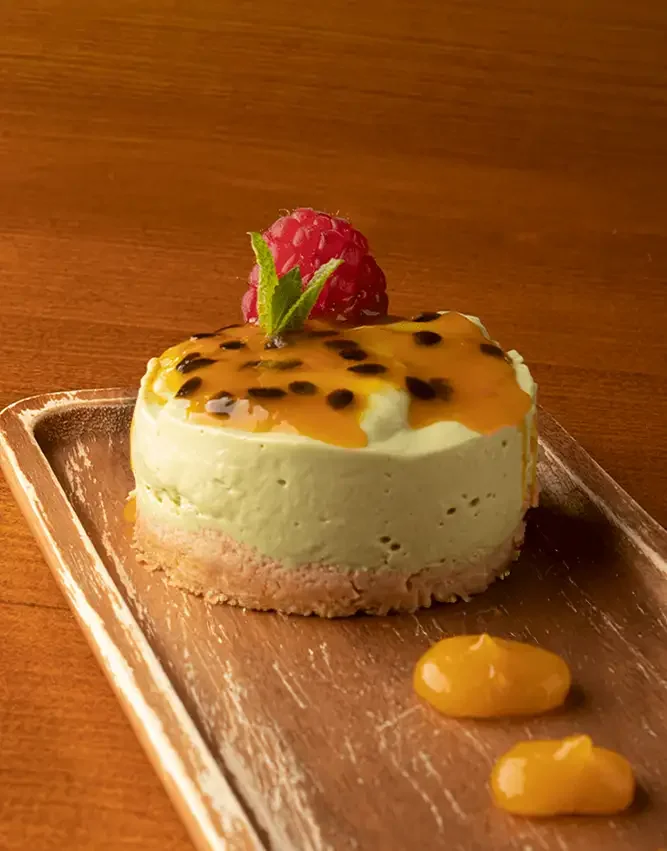 Tarta de queso con salsa de maracuya, decorada con frambuesa y menta, en plato de madera