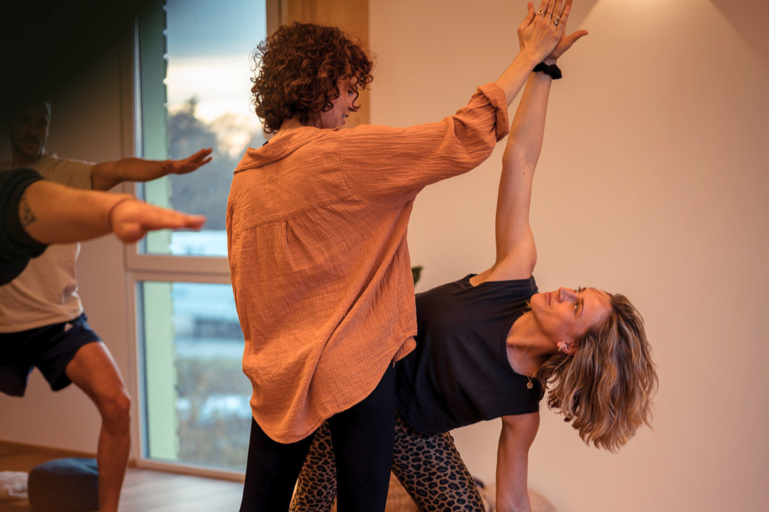 Zwei Frauen und ein Mann machen Yoga- oder Entspannungsübungen in einem Raum mit Fenstern.