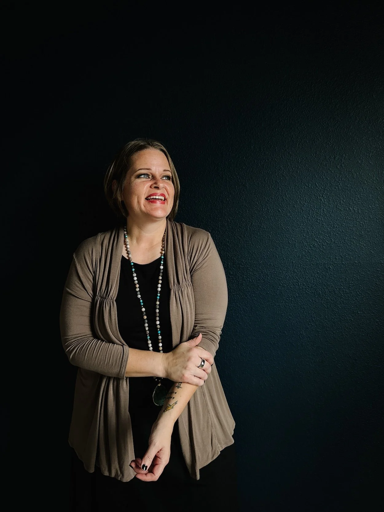 Smiling white woman holding arm. Dark background.