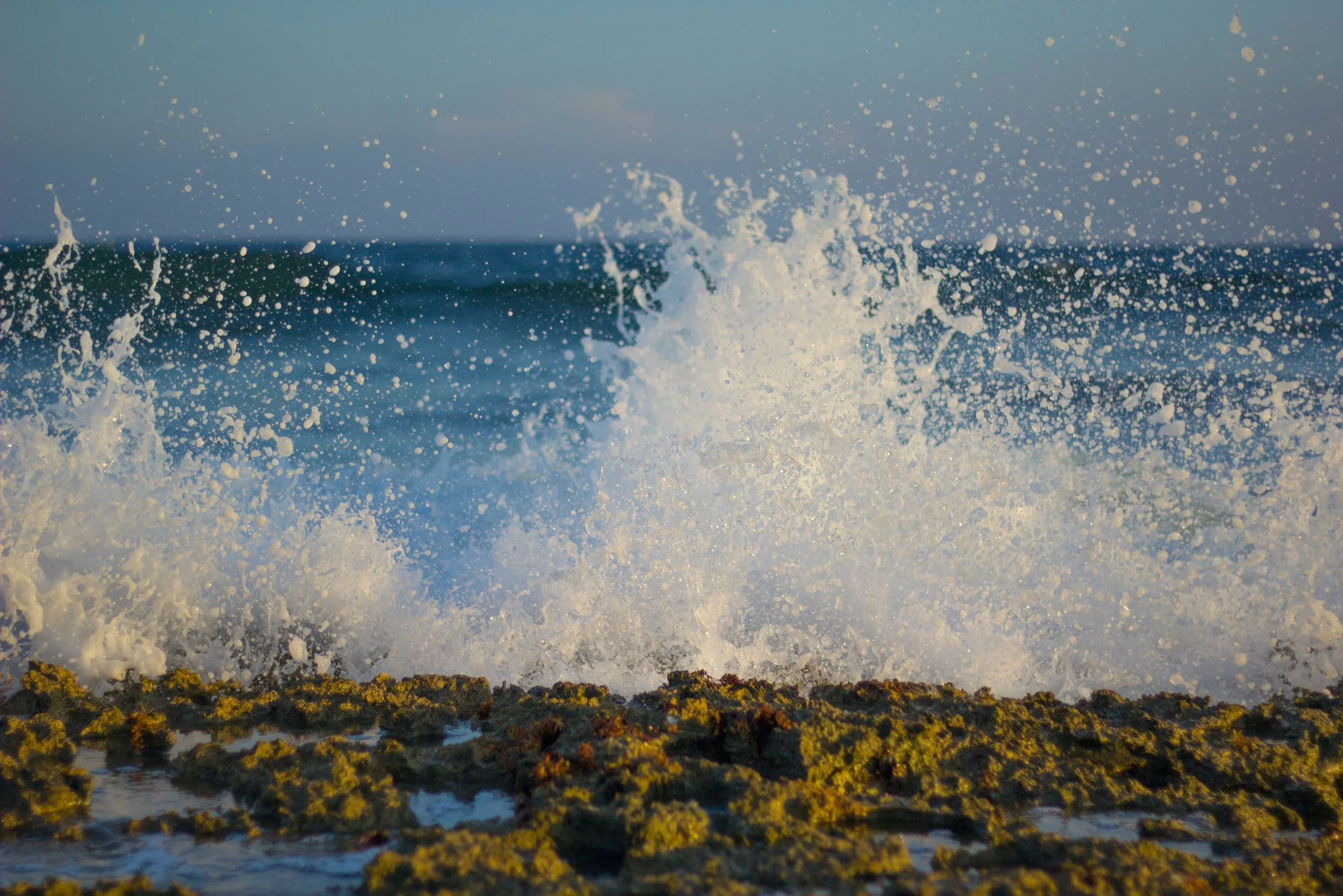 Waves crashing onto a rocky shoreline with water spray in the air during daytime.