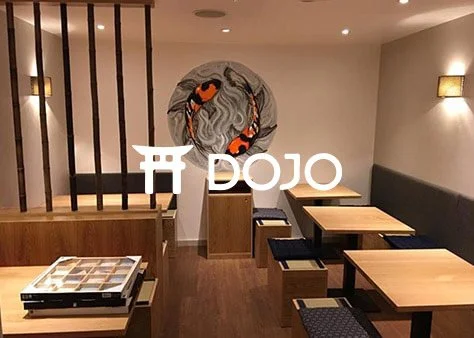 Interior of a Japanese restaurant with tables, benches, and a decorative circular wall feature with carp fish.