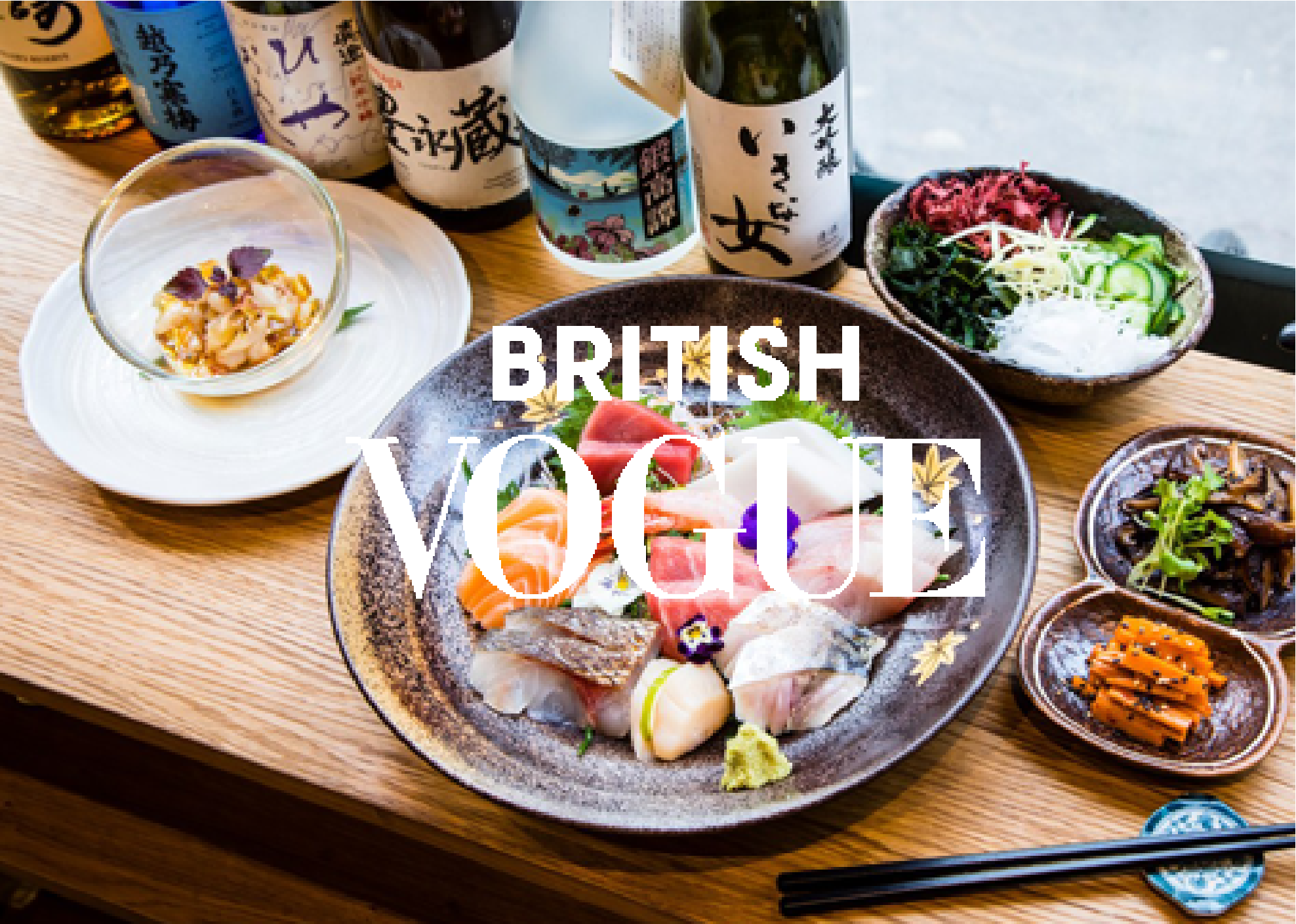 Assorted Japanese dishes including sashimi, salads, and small side dishes, with bottles of sake in the background, on a wooden table.
