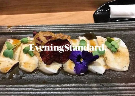 Seared fish fillet garnished with edible flowers and microgreens on a black rectangular plate.