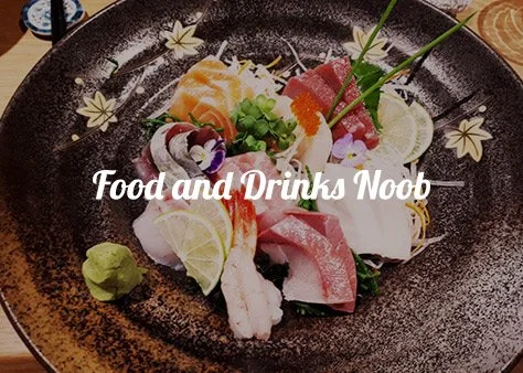 A black plate of assorted sashimi garnished with lime, wasabi, and greens, with floral decorations.