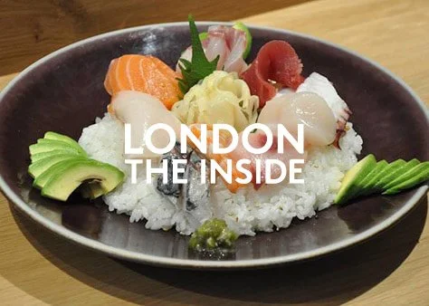 Assorted sashimi and rice on a black plate, garnished with green avocado slices and wasabi.