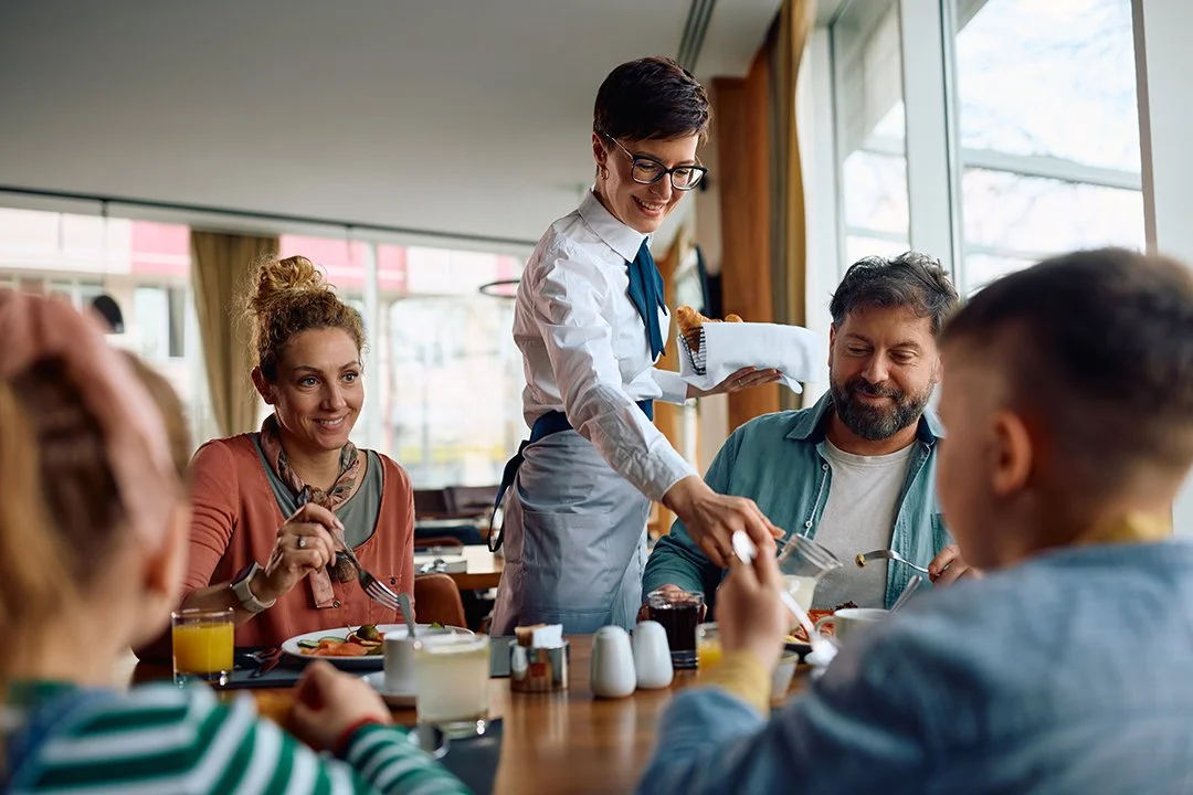 happy-hotel-waitress-serving-family-who-is-having-2026-03-17-07-06-27-utc.jpg