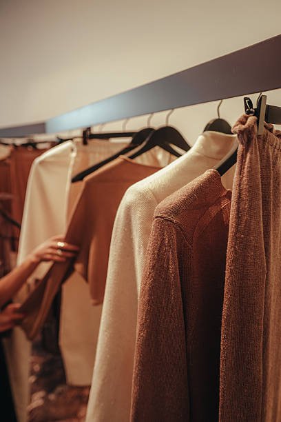Clothes hanging on a rack in neutral and earthy tones, including sweaters and shirts.
