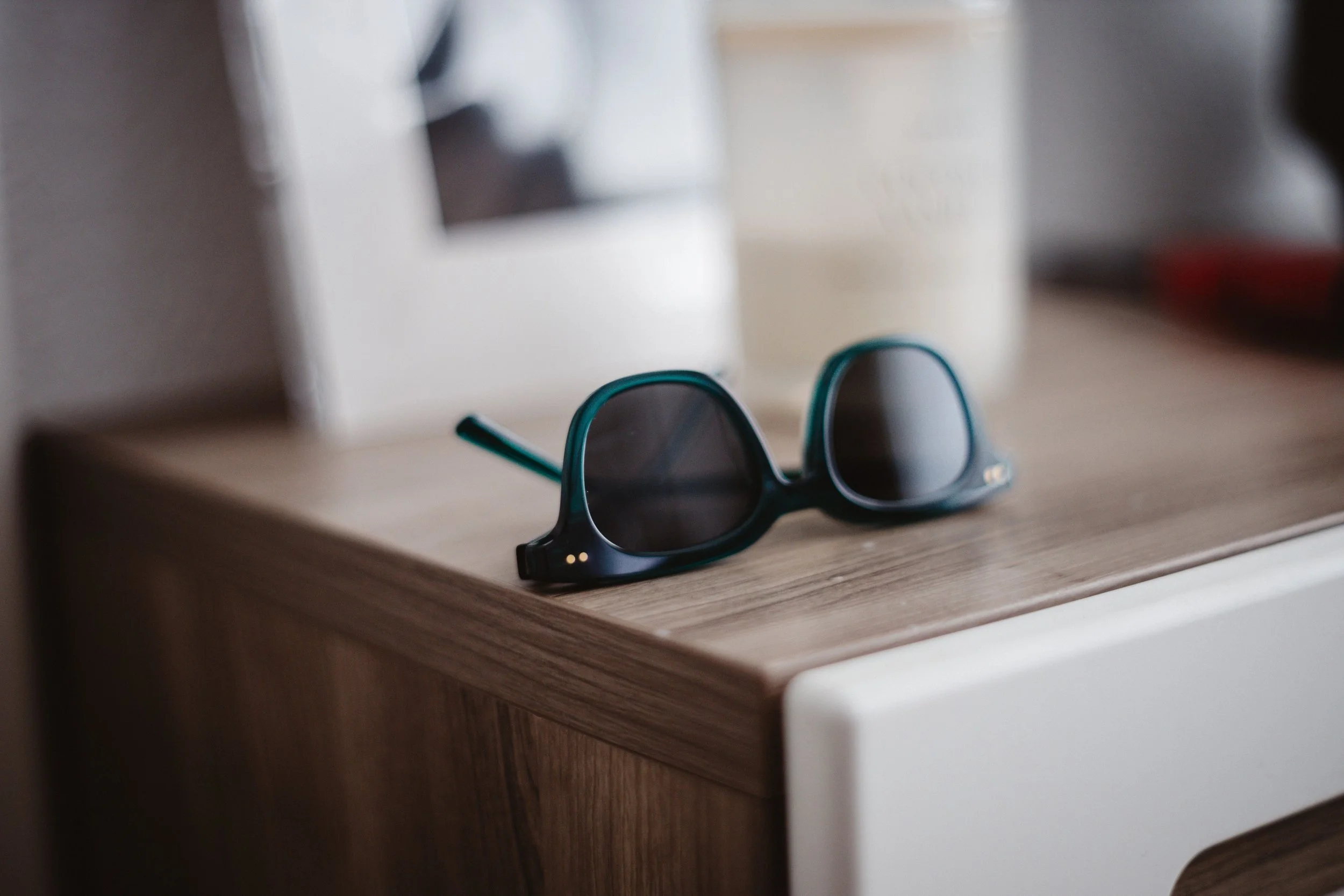 Black sunglasses resting on a wooden console table, with blurred objects in the background.