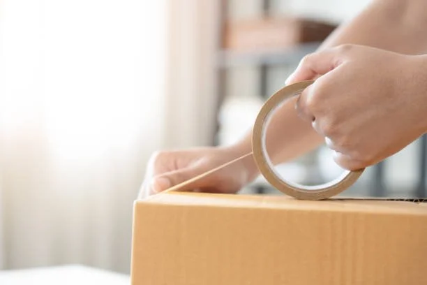 Person sealing a cardboard box with packing tape.