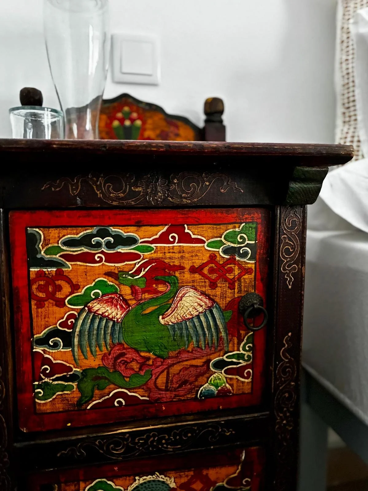 Close-up of a colorful wooden cabinet featuring an Asian-style painting of a green bird with pink wings, surrounded by clouds and decorative patterns.