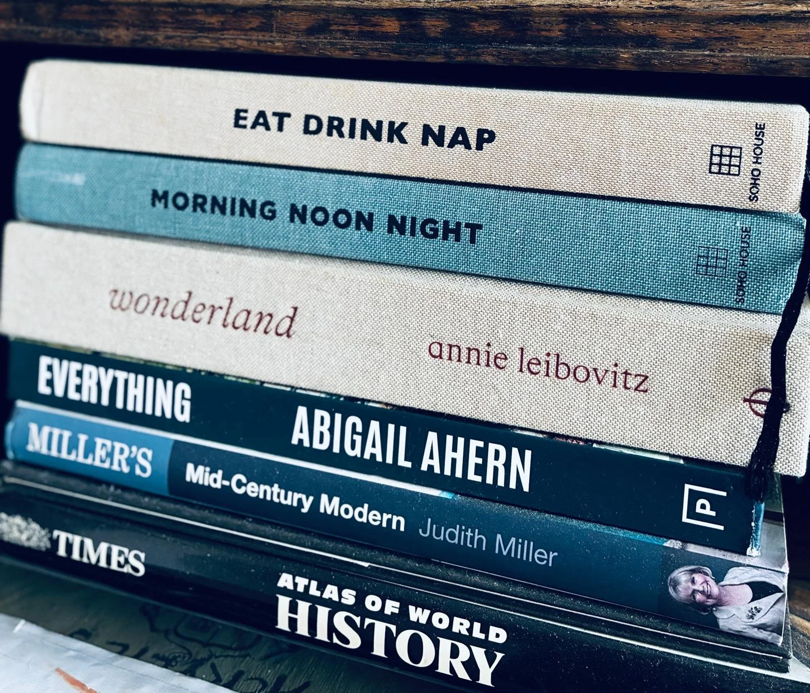 Stack of books with titles including "Eat Drink Nap," "Morning Noon Night," "Wonderland" by Annie Leibovitz, "Everything" by Abigail Ahern, "Mid-Century Modern" by Judith Miller, and "Atlas of World History."