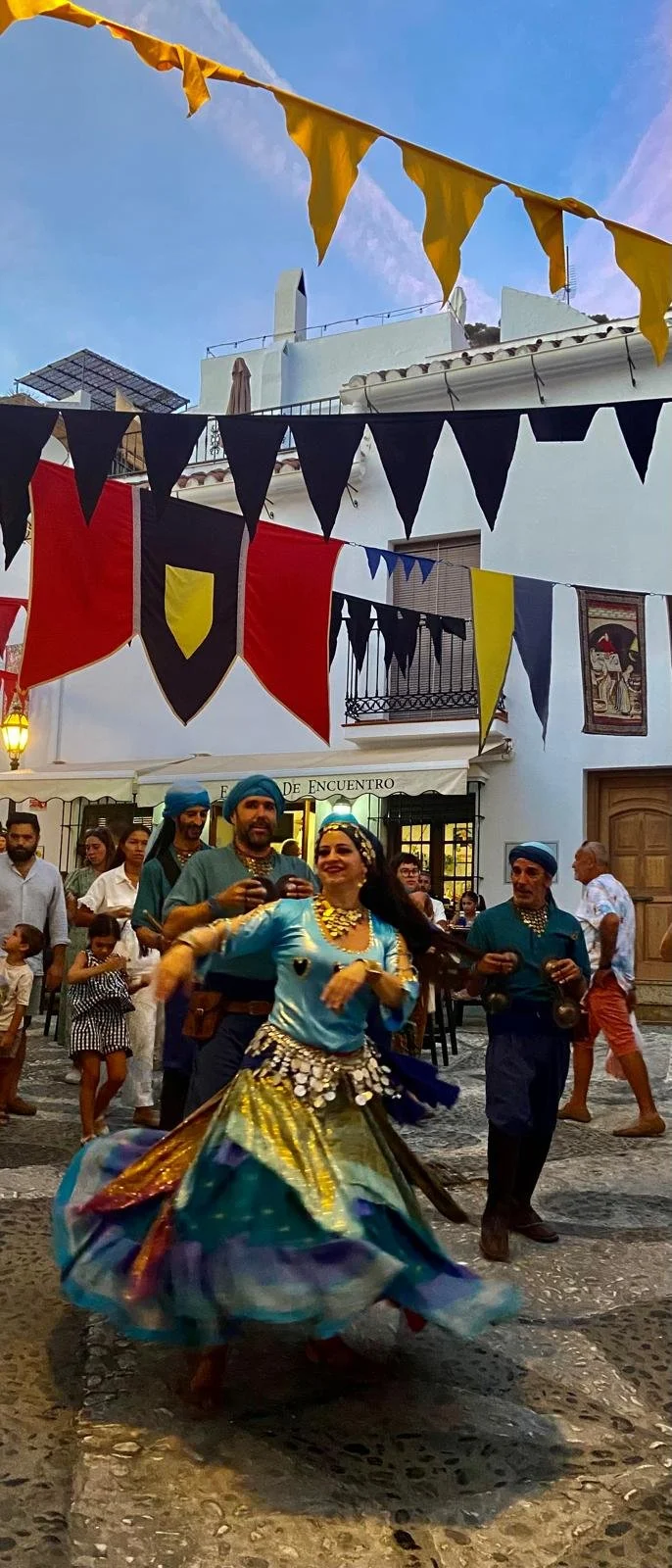 People dancing in traditional colourful attire during the 3 culturas street festival, with flags and crowd in the background.