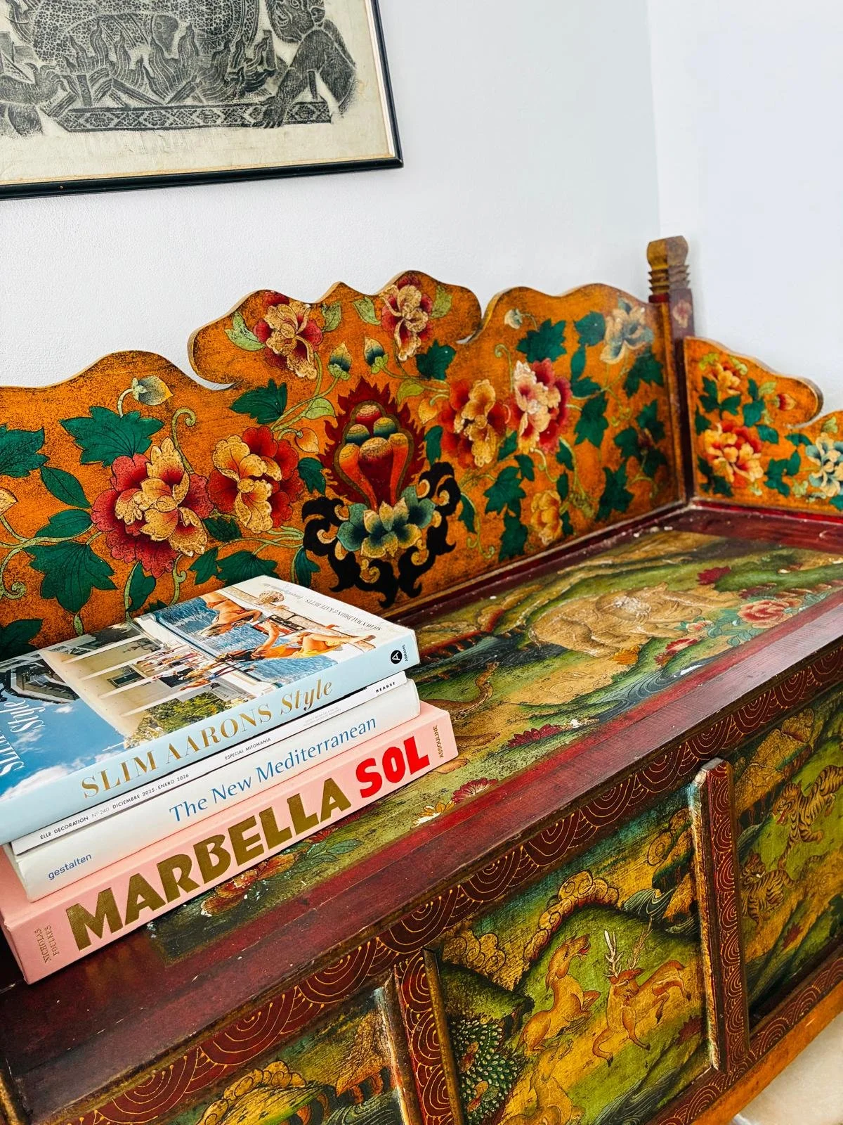 A colorful, intricately painted wooden cabinet with floral and mythical motifs, topped by three books about Mediterranean style and design.