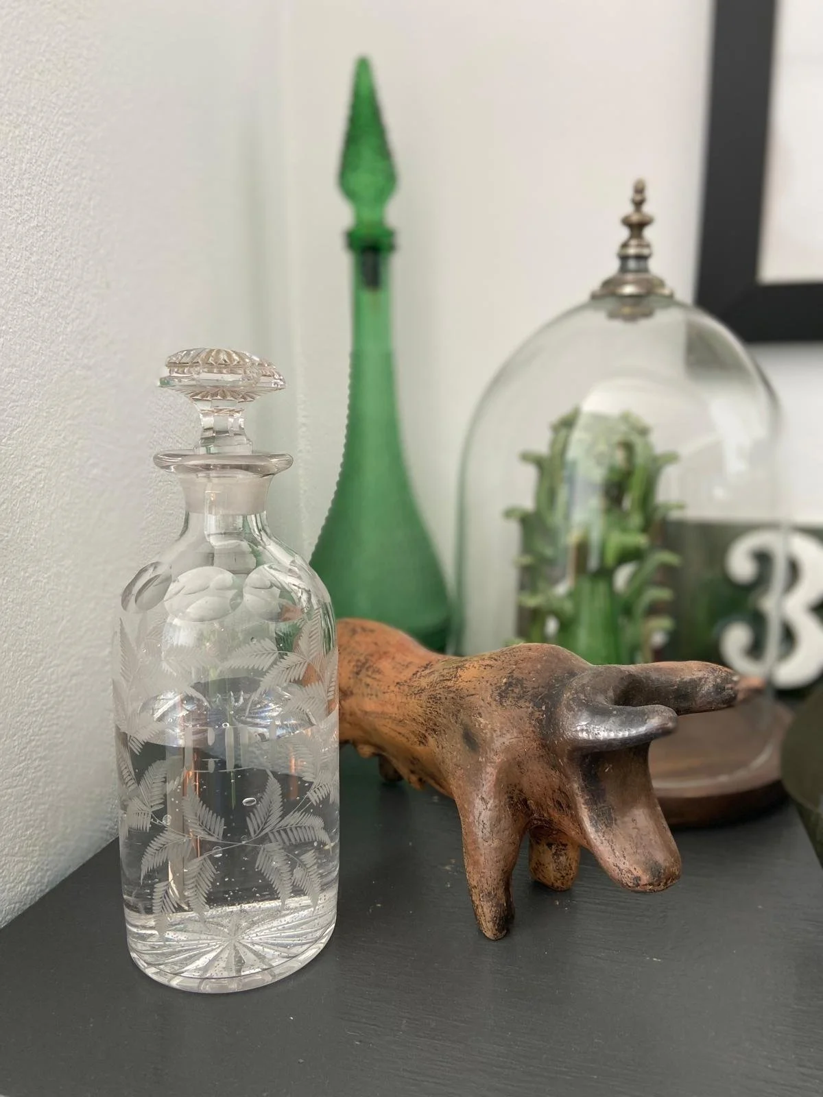 Decorative glass bottle with etched leaf design, wooden animal figurine, and various glass and ceramic decorative objects on black surface.