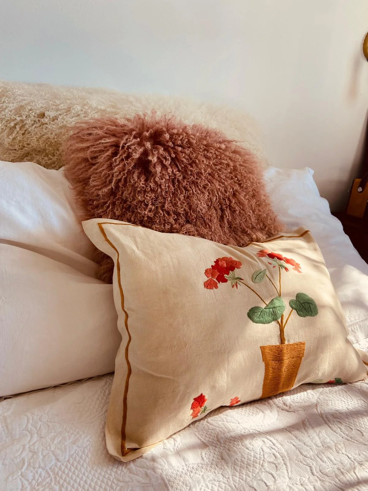 A bed with decorative pillows featuring embroidery of red flowers and green leaves in a vase.