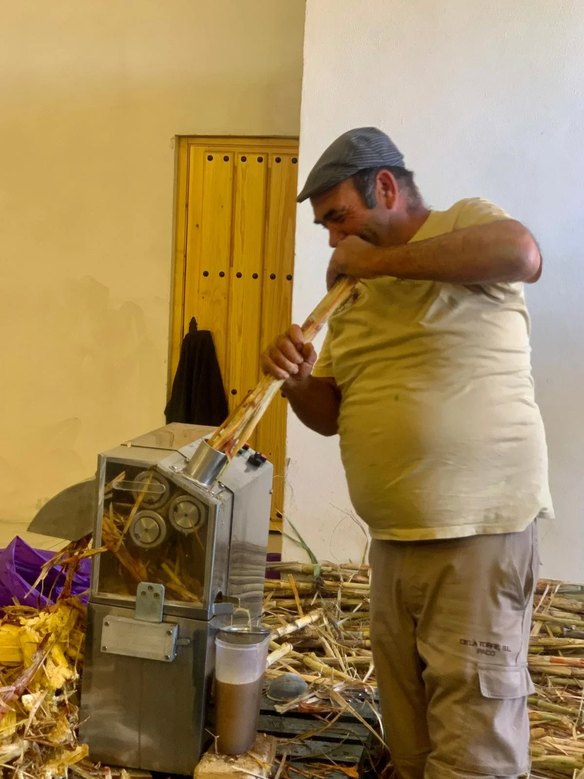 A man operating a sugarcane juicer machine, feeding sugarcane stalks into the machine's input.