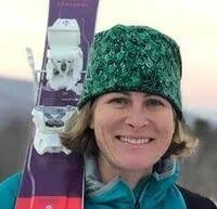 Smiling woman wearing a green knit hat holding skis over her shoulder