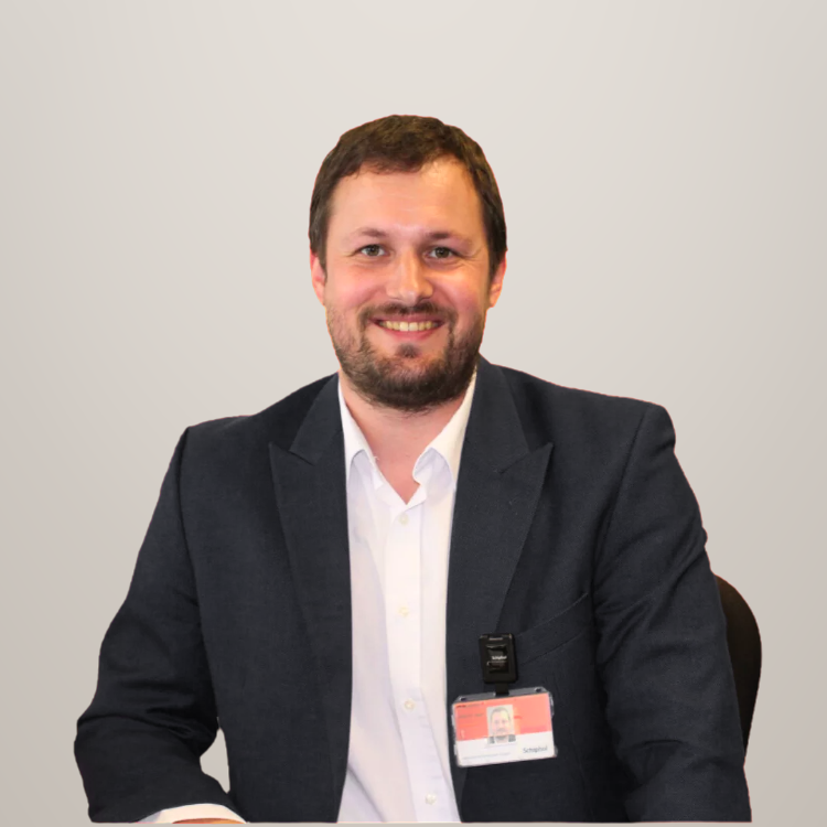 Man in een zwart pak en wit overhemd zit aan tafel en glimlacht.