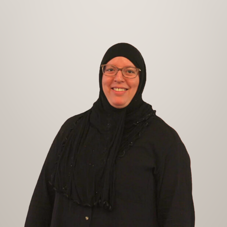 Vrouw met hoofddoek en bril die glimlacht op een lichte achtergrond.