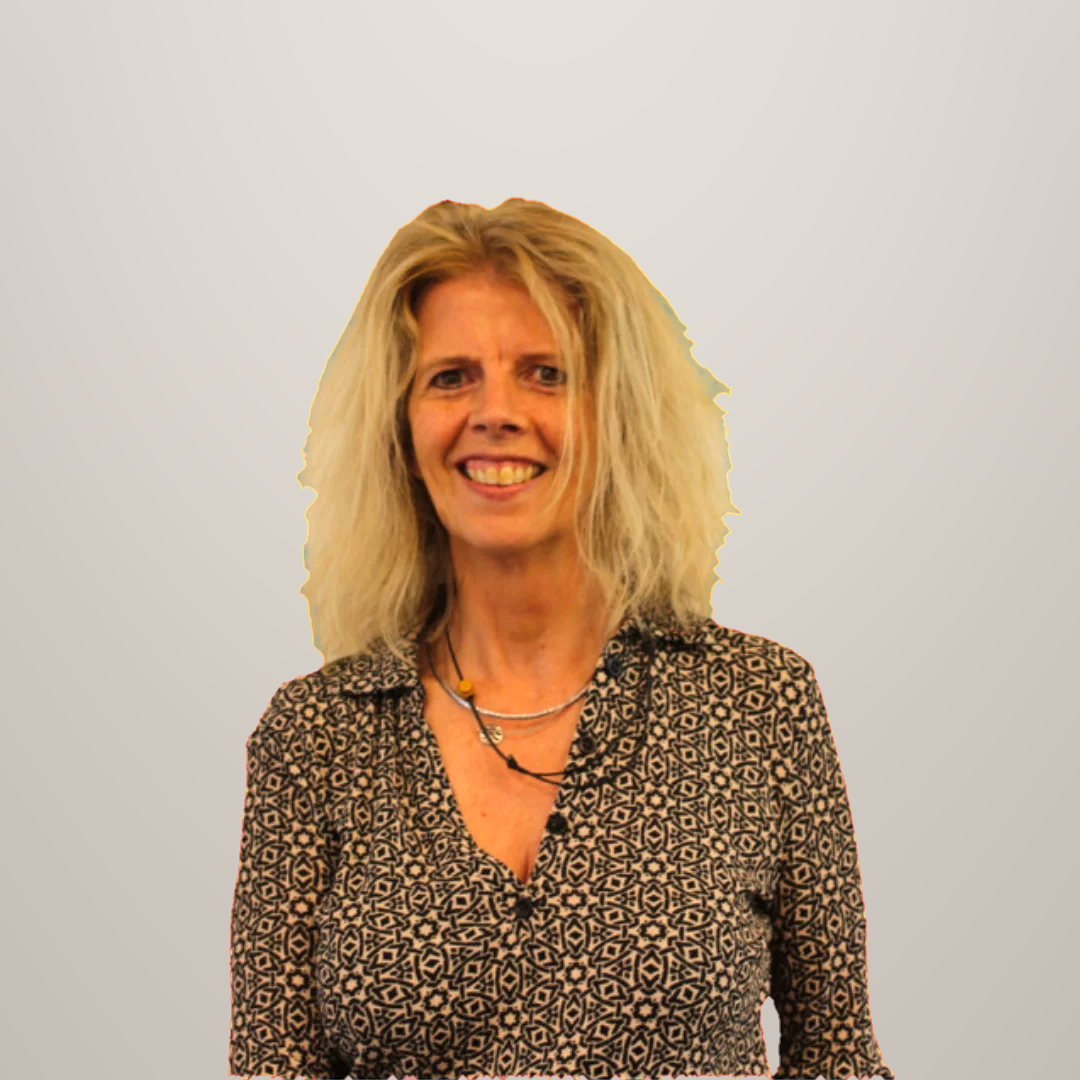 Een vrouw met blond, golvend haar, lachend en gekleed in een blouse met een patroon.