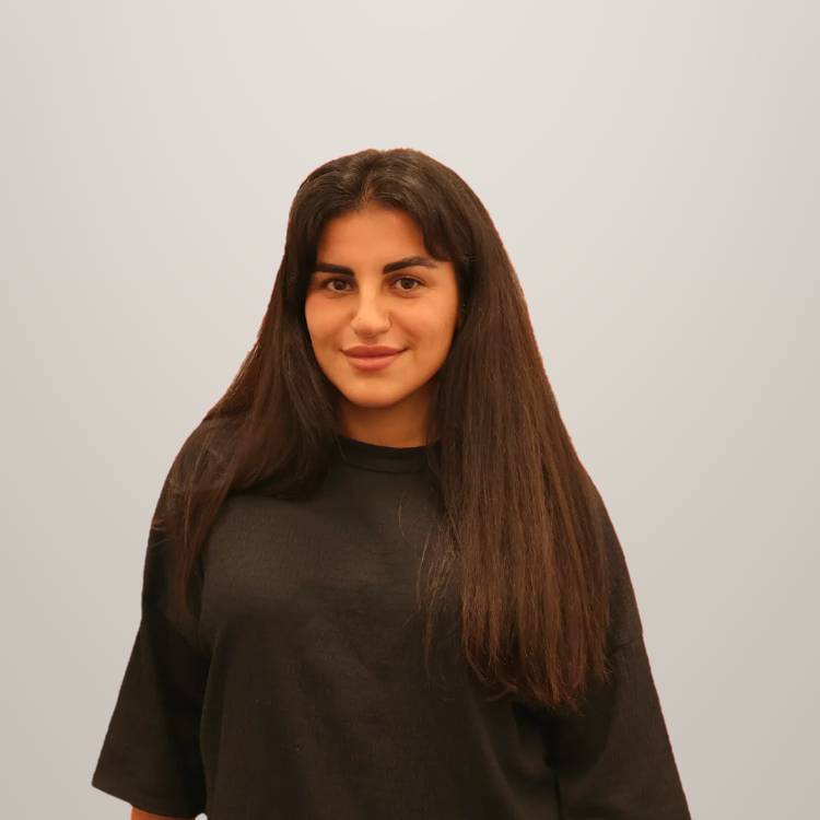 Portret van een vrouw met lang bruin haar, gekleed in een zwart shirt, lachend en voor een lichte achtergrond.