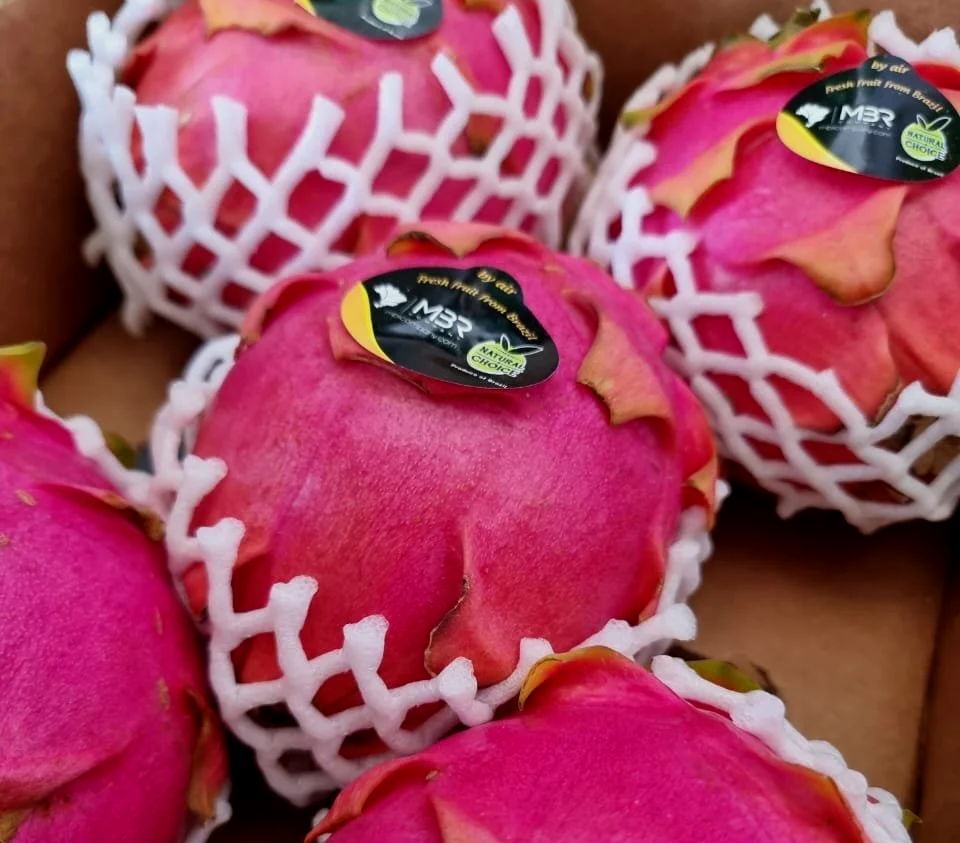 Pêssegos rosa envoltos em redes de proteção branca, com etiquetas de origem e qualidade.