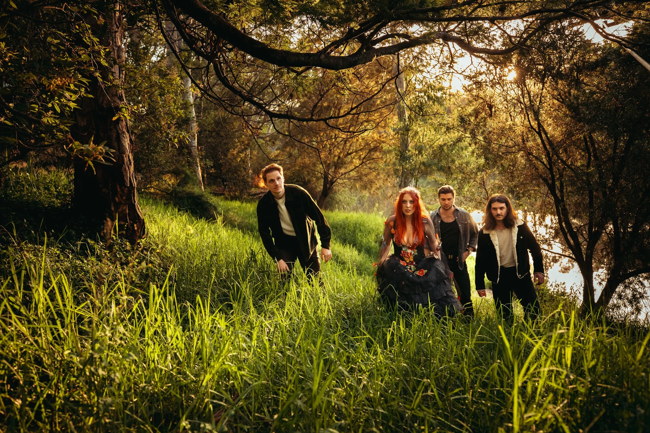 Four people walking through a lush, green forested area during sunset, with sunlight filtering through the trees.