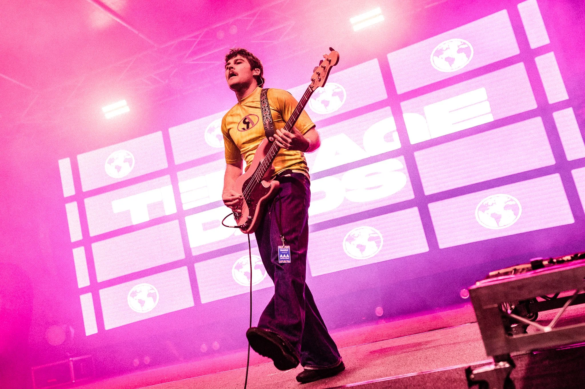 A man playing a guitar on stage with a pink background displaying a globe logo and text.