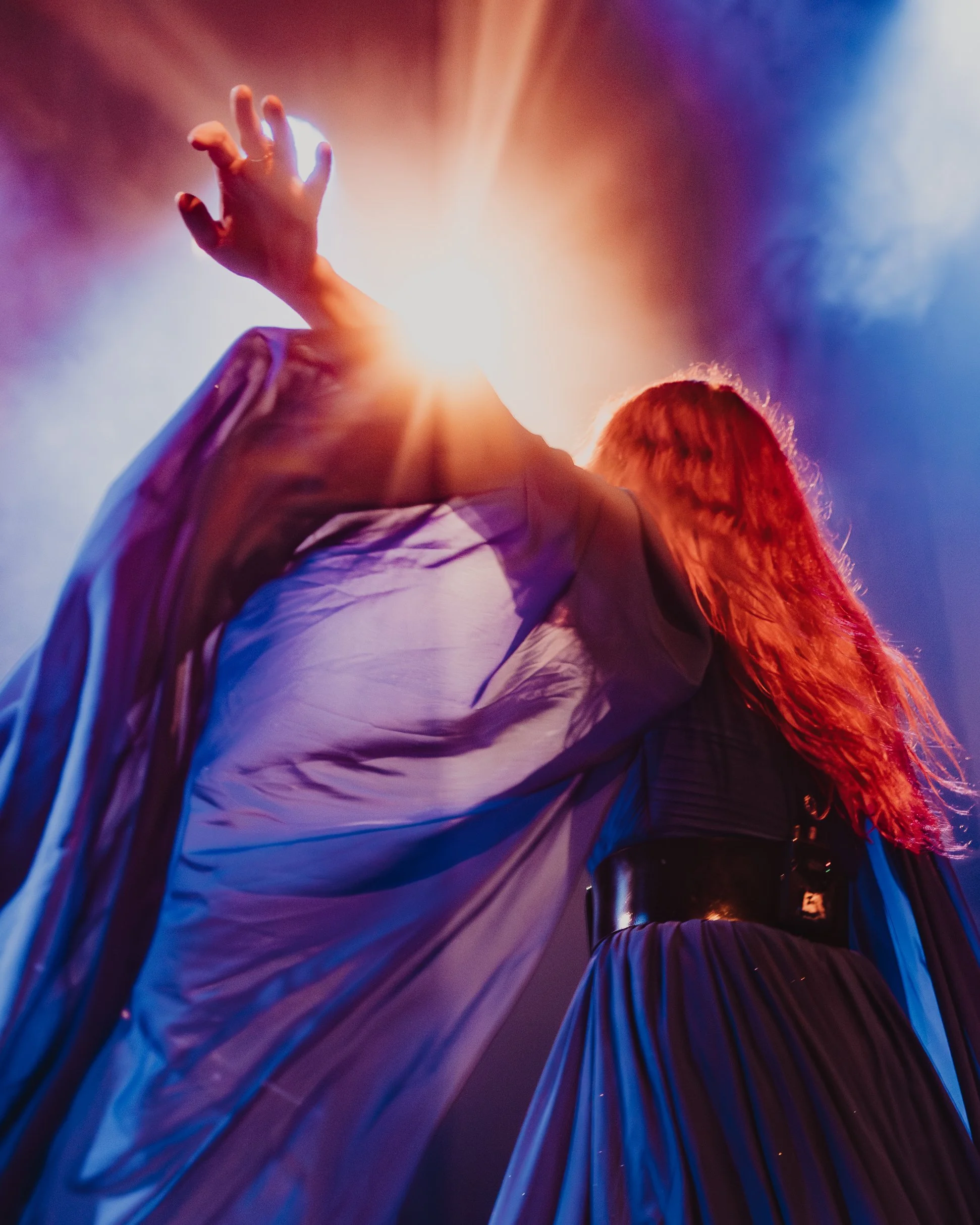 Close-up of a person's hand reaching out, with colorful stage or party lights in the background, creating a vibrant and energetic atmosphere.