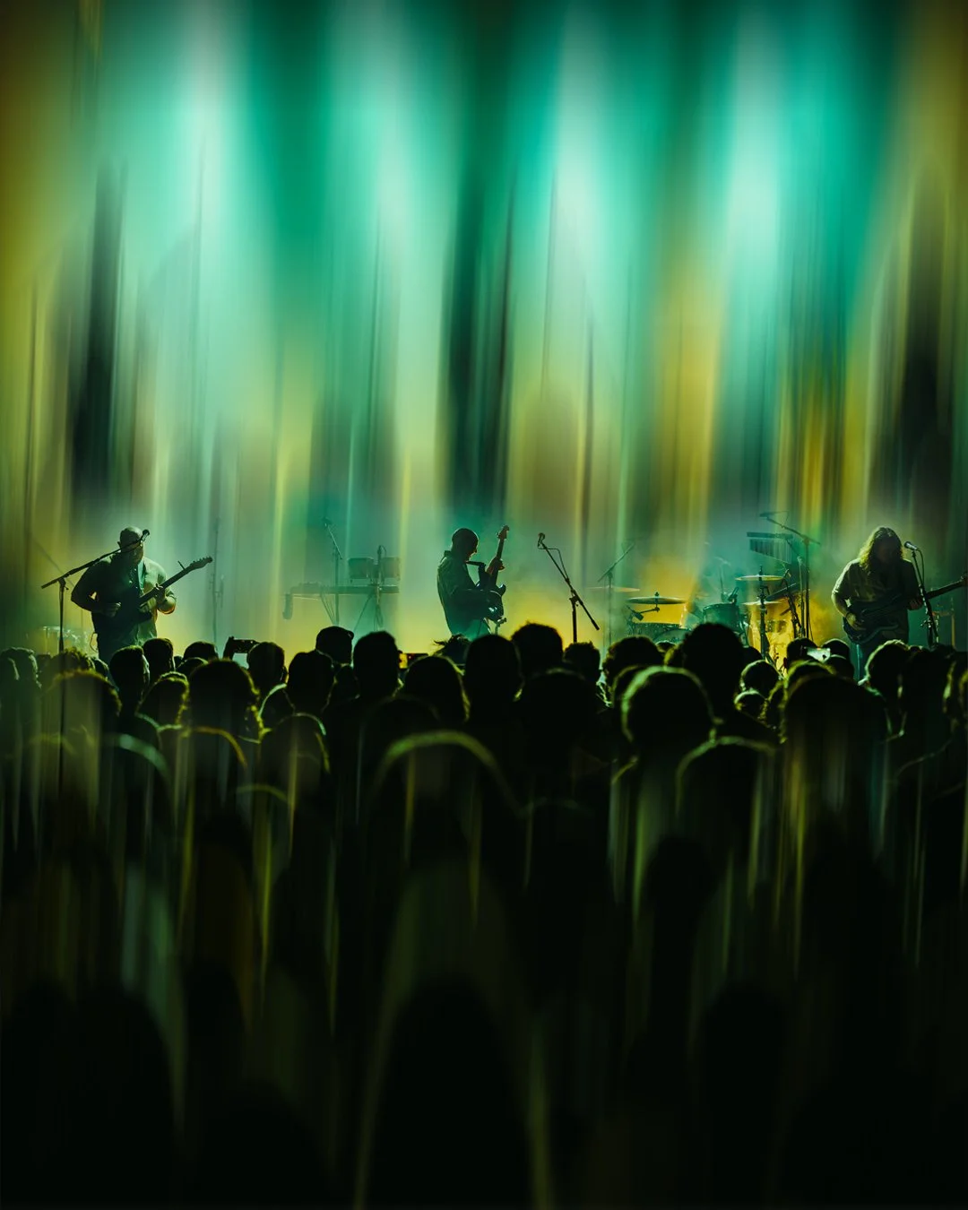 A musical band performs on stage with vibrant green and yellow lighting, viewed from the audience.