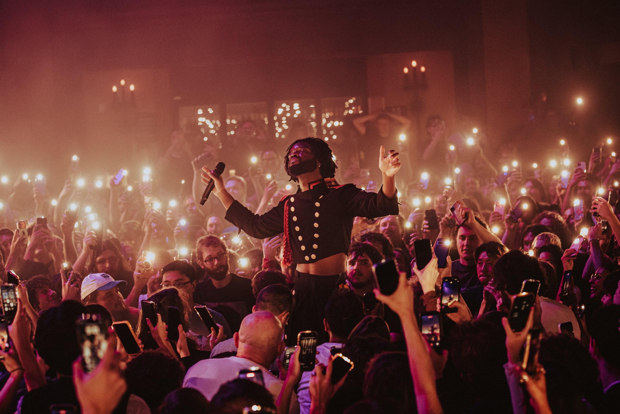 A performer singing on stage surrounded by an audience holding up illuminated phones during a concert.