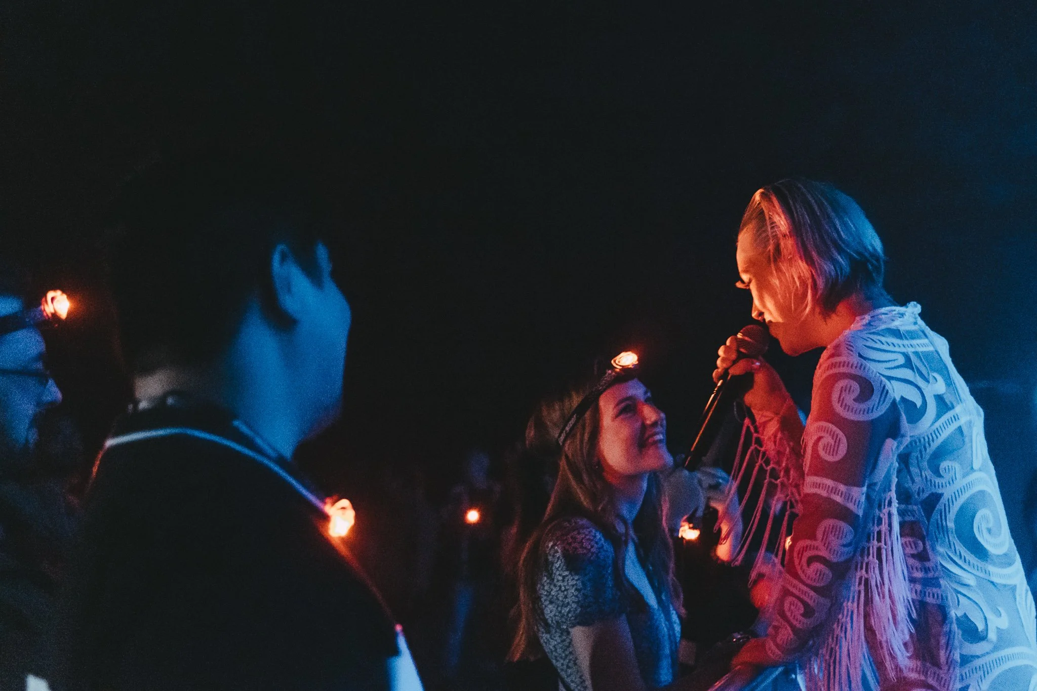 Group of young people at night holding sparklers, smiling and interacting with a singer or performer holding a microphone.