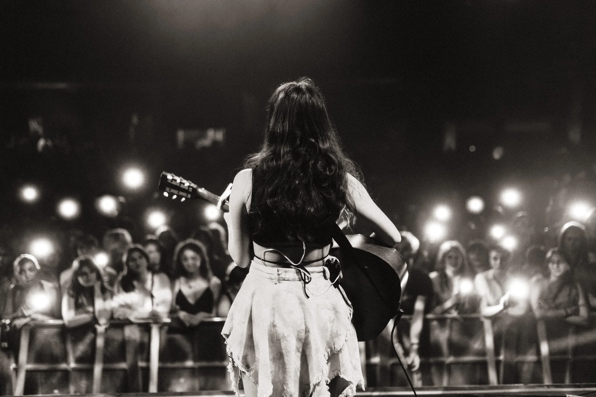A woman with long wavy hair playing a guitar on stage in front of an audience at a concert or event.