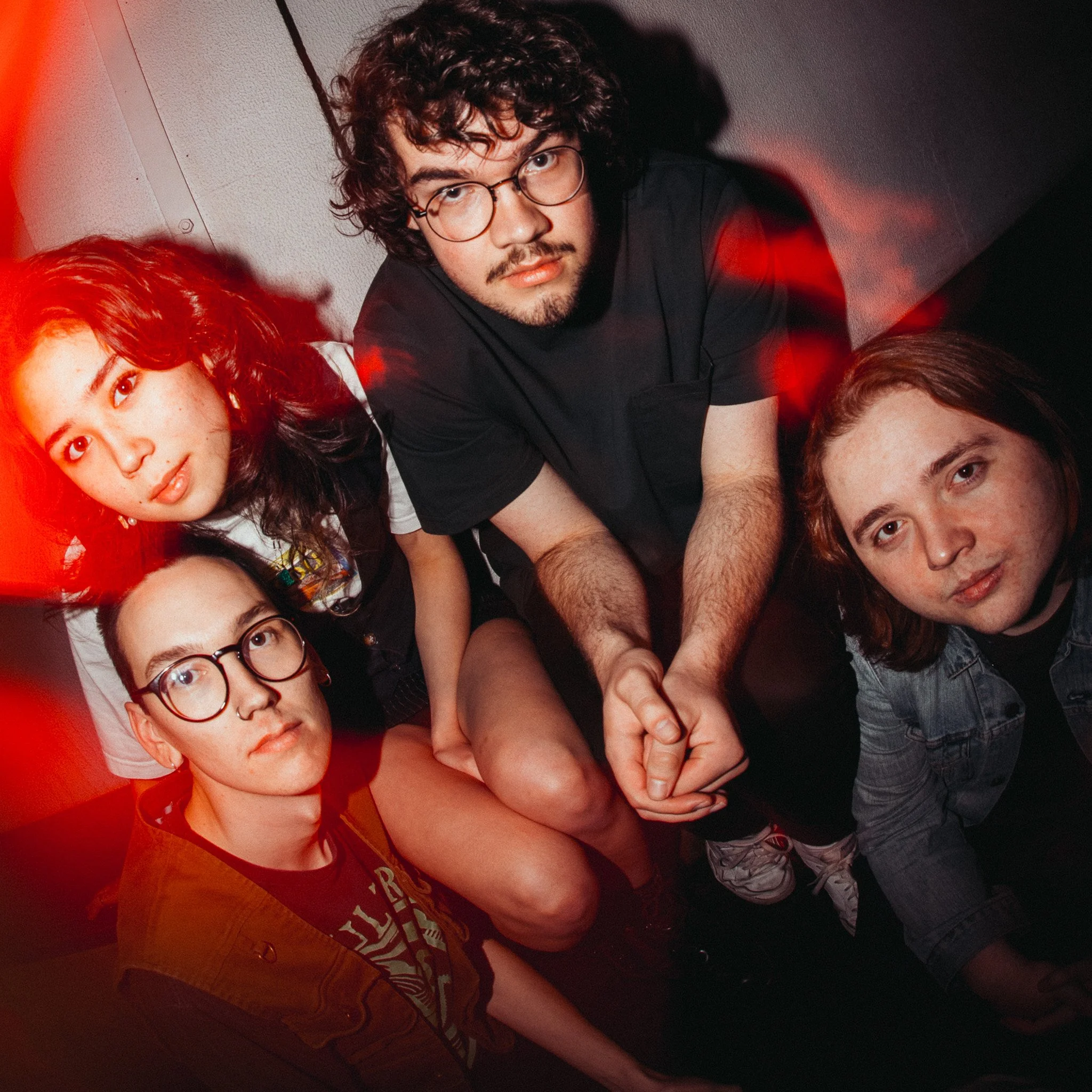 A group of young people posing for a photo in a dimly lit room with red lighting. The photo is taken from above, showing their faces and part of their bodies.
