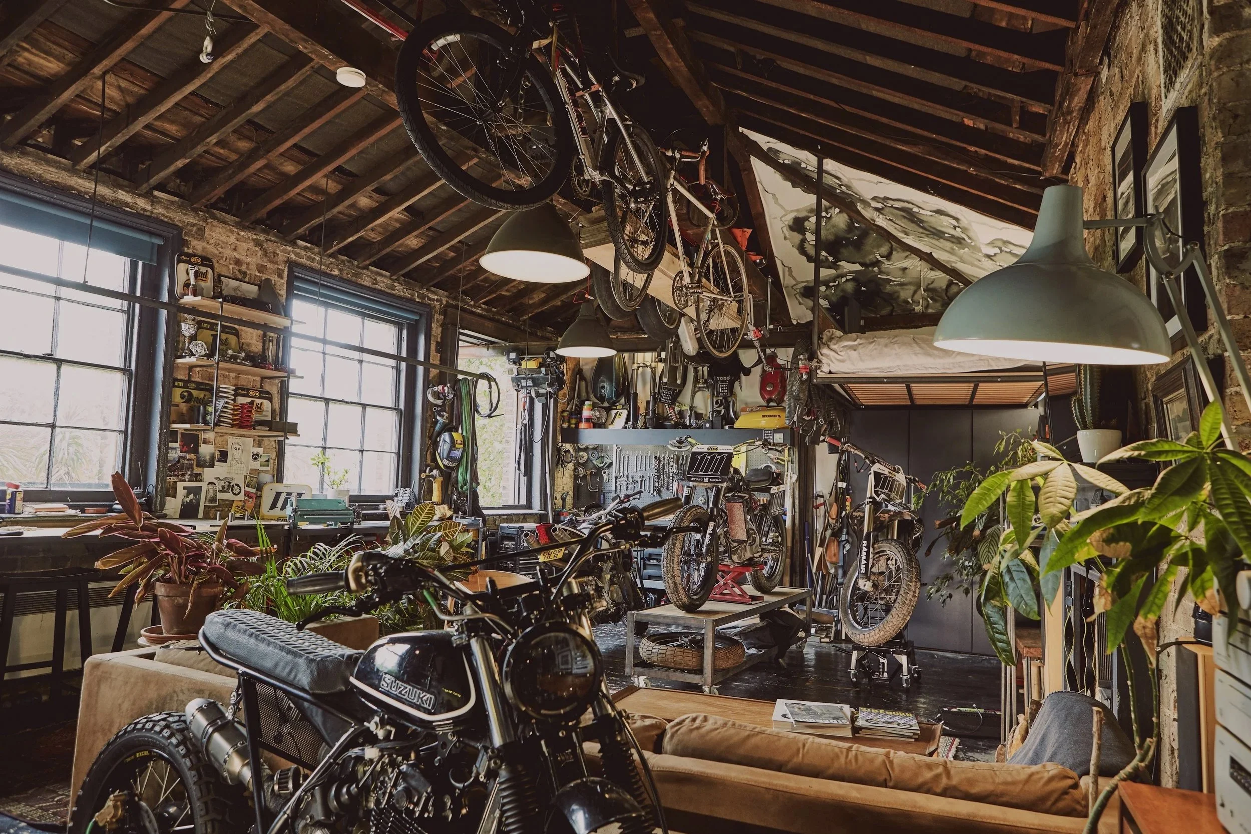 Interior of a rustic bike workshop with bicycles hanging from the ceiling, plants, and tools.