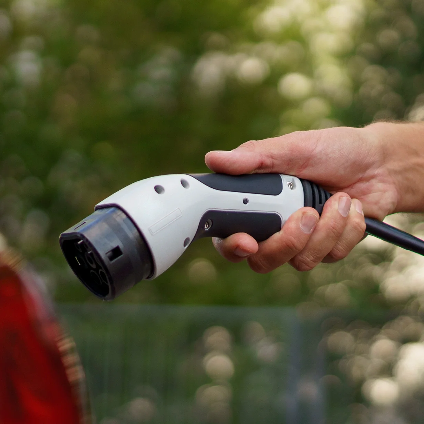 Ein Hand hält eine Ladestation für ein Elektroauto, bereit zum Aufladen.