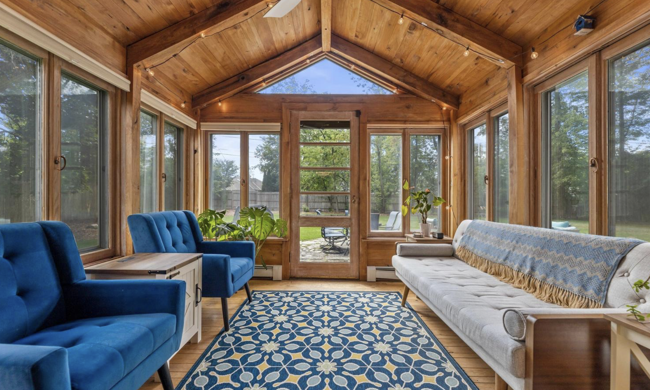Sunroom with wooden ceiling and walls, large windows, blue and white furniture, and a patterned rug.
