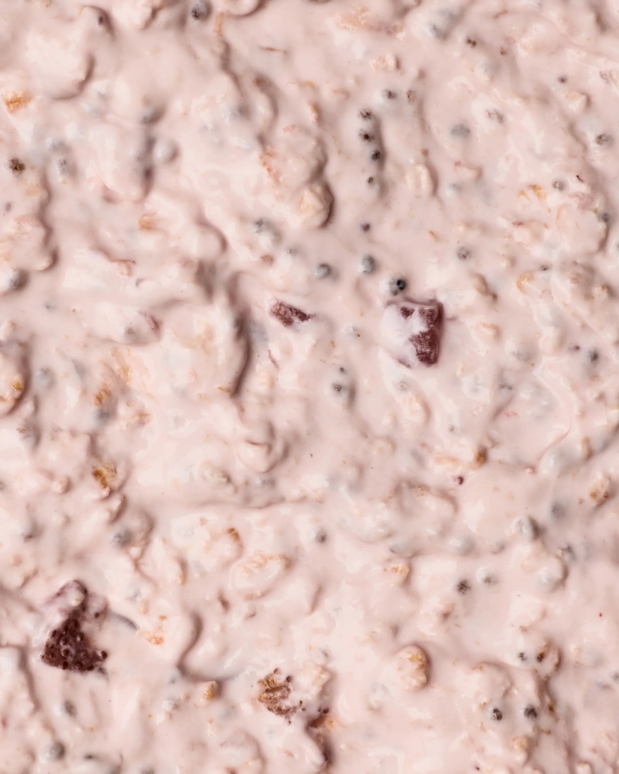 Close-up of a creamy mixture with small dark specks and chunks, possibly a dessert or food preparation.
