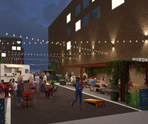 Night scene of an outdoor urban space with people socializing, sitting at tables, and walking. String lights hang overhead, and buildings surround the area. There is a sign that reads 'Huron'.
