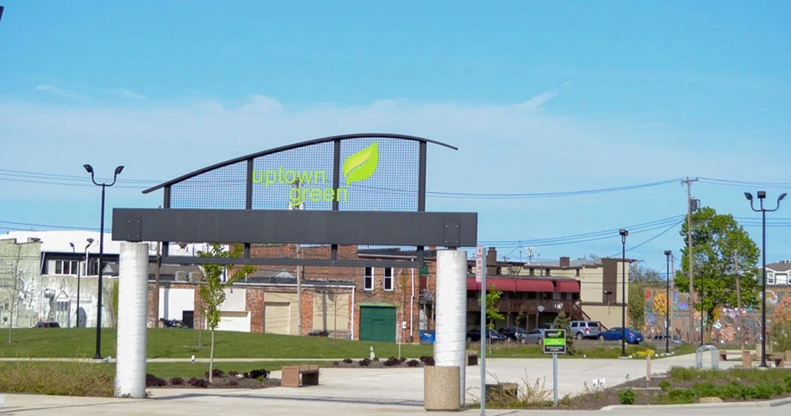 Entrance sign to Uptown Green with a leaf logo on a cloudy day