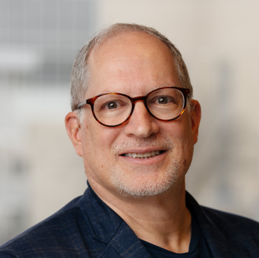 A middle-aged man with glasses and gray hair smiling in an office setting.