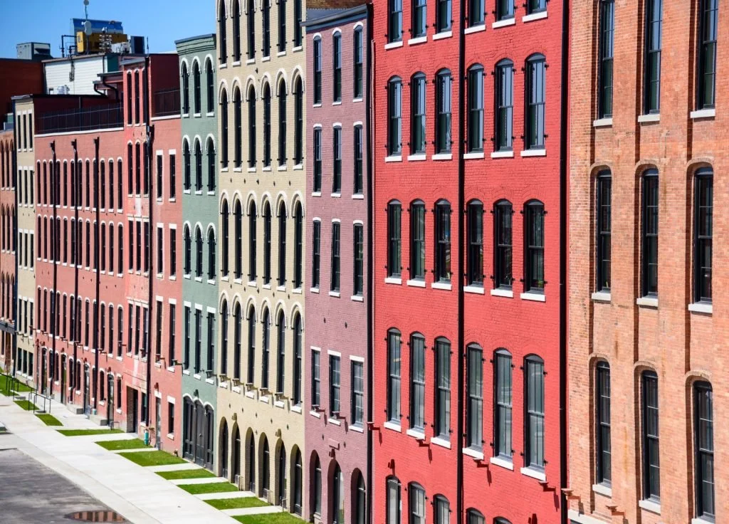 Colorful multi-story brick apartment buildings with arched windows lining a sidewalk under a clear blue sky.