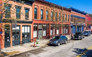 Row of colorful historic buildings with storefronts and parked cars on a city street under a clear blue sky.