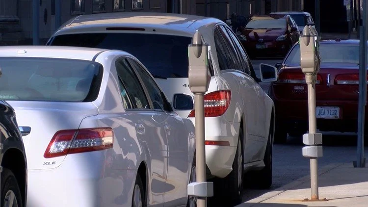 Several parked cars along the street with a white parking meter in the foreground.