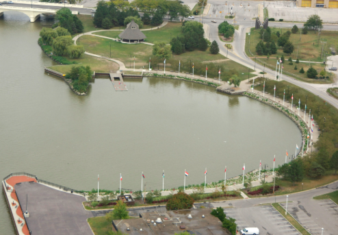 A pond with a curved shape surrounded by a landscaped park, walking paths, and a small gazebo, with flags along the shoreline.